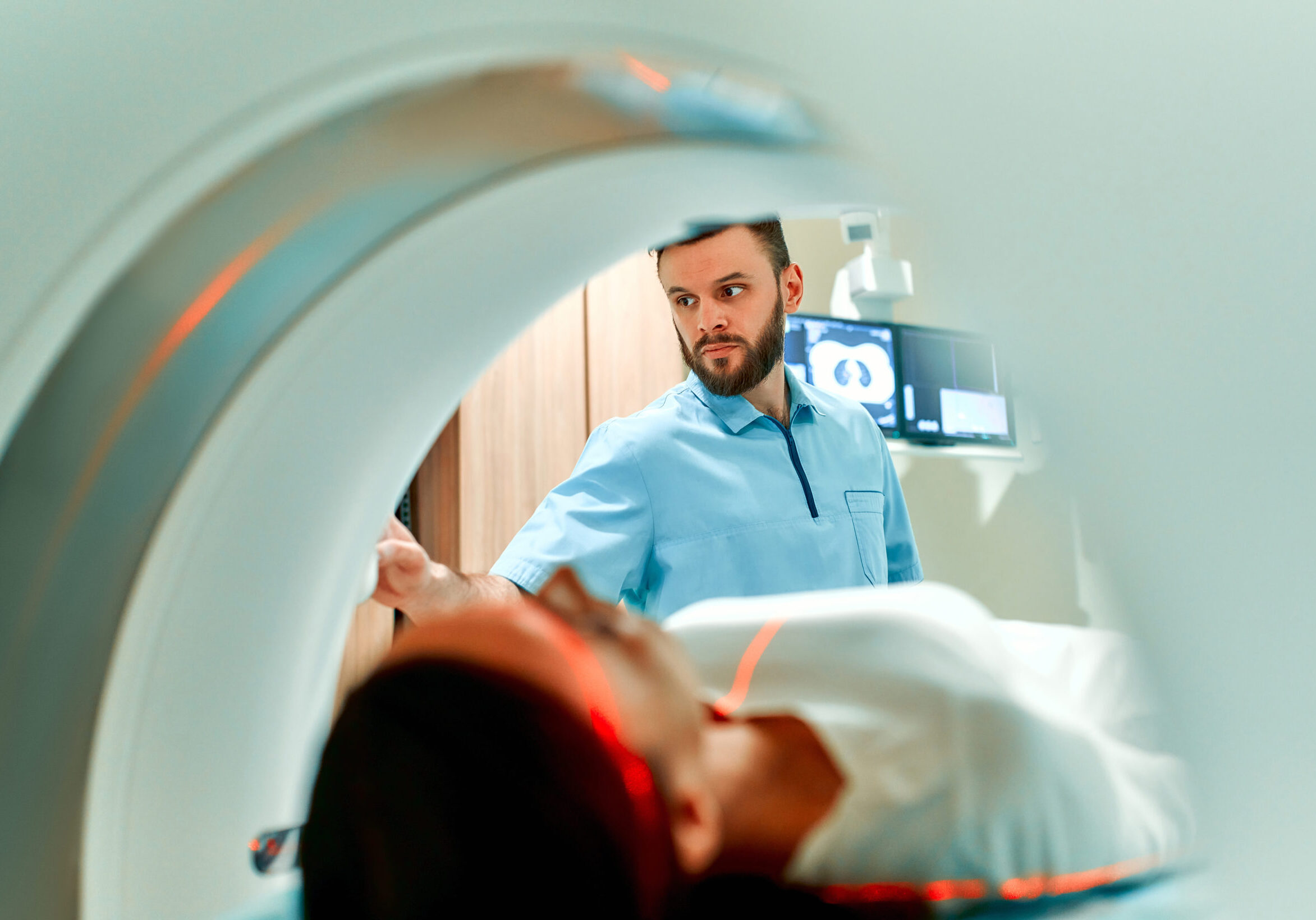 A patient lying on CT or MRI, the bed moves inside the machine, scanning her body and brain under the supervision of a doctor and a radiologist. In a medical laboratory with high-tech equipment.